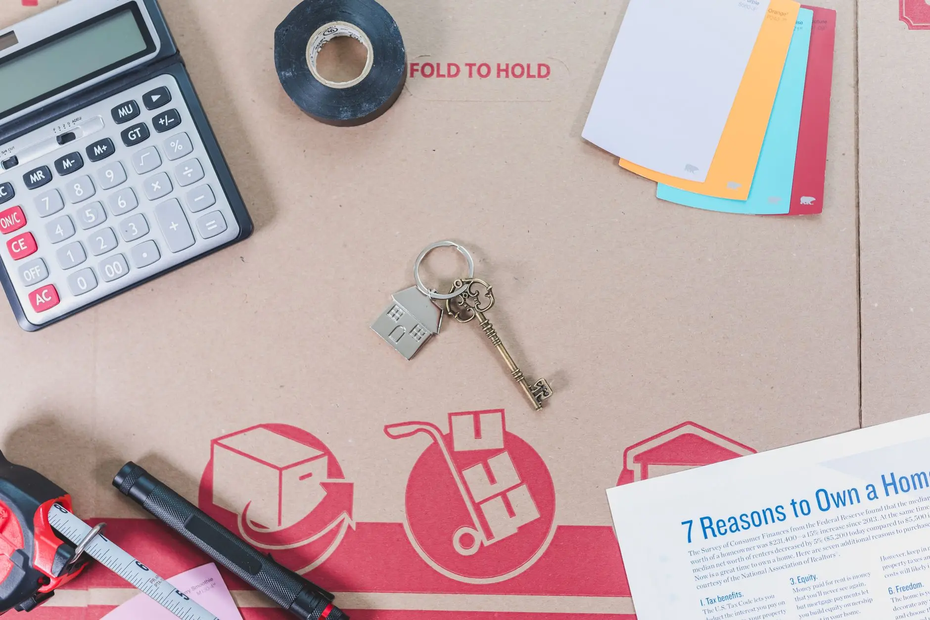 Flat lay of home buying essentials with calculator, keys, tape, and color swatches.